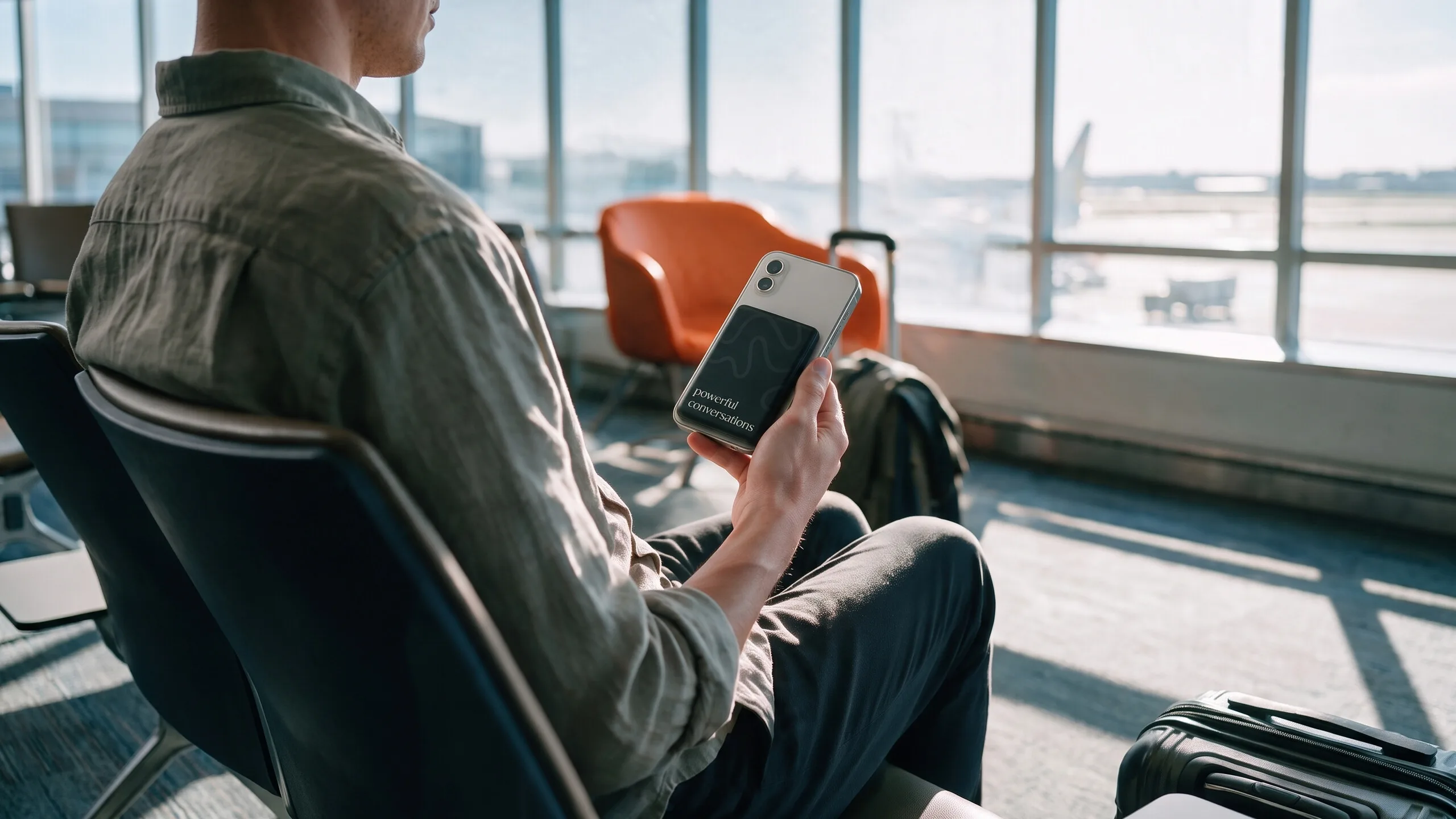 Man in airport lounge holds phone with a black card reading "powerful conversations".