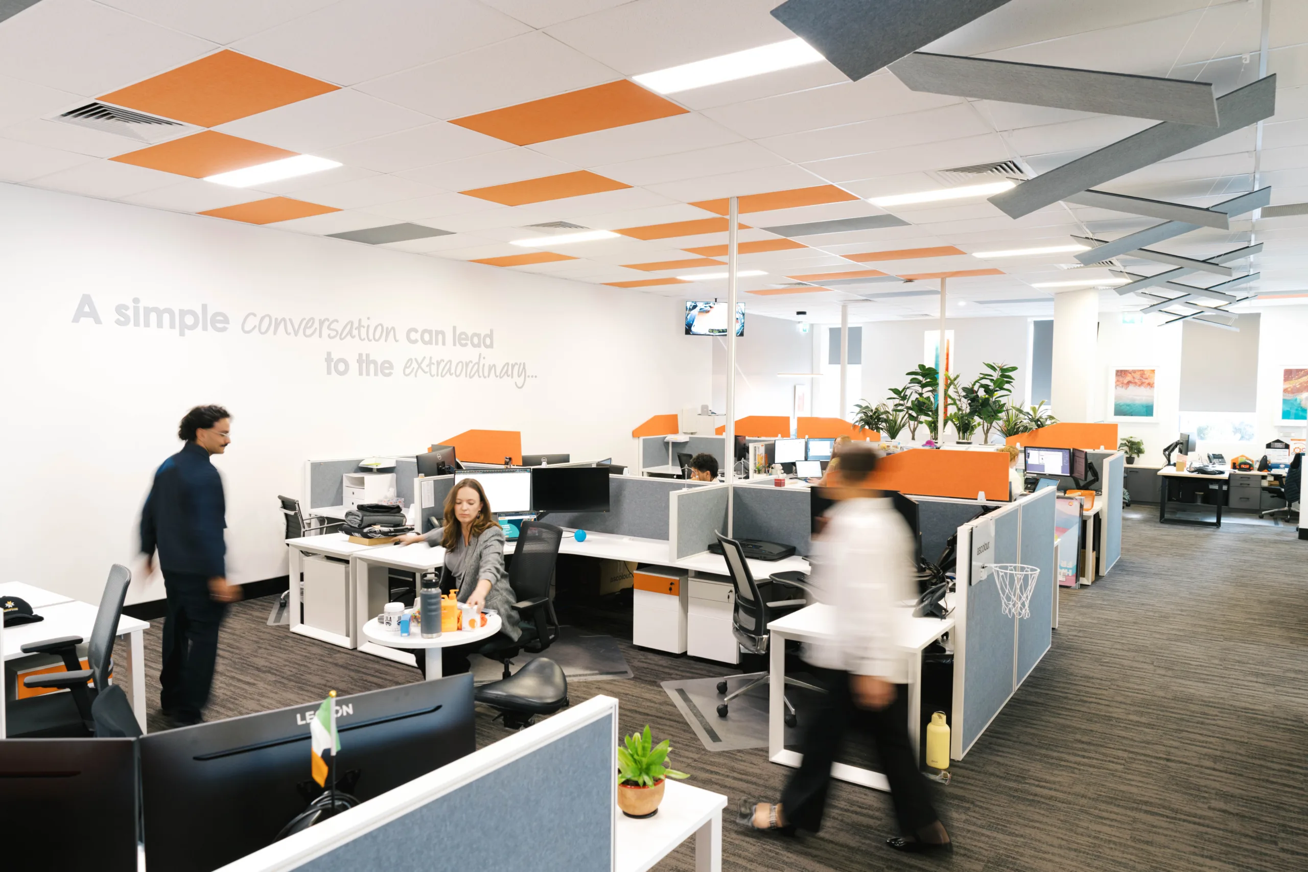 Modern office space with people working at desks and a motivational quote on the wall.