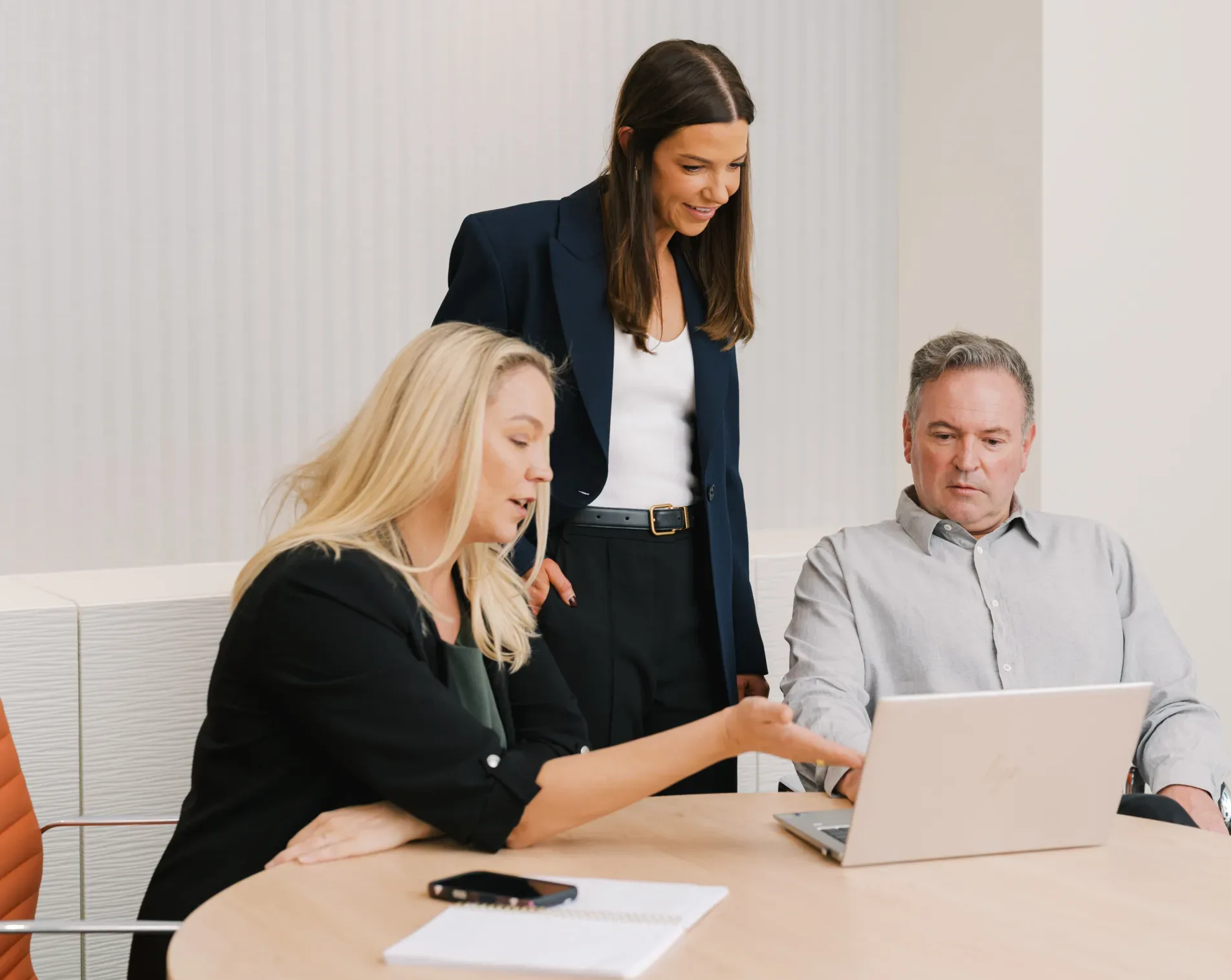 Three professionals in a meeting reviewing information on a laptop.