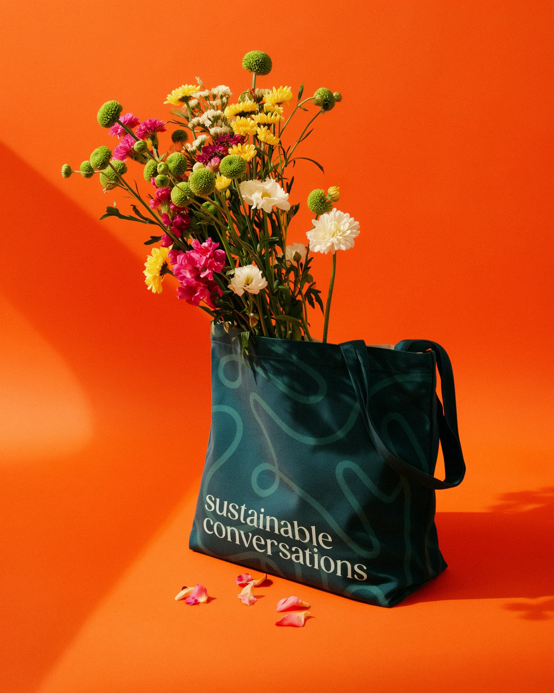 A teal tote bag with the words "sustainable conversations" printed on it, filled with a bouquet of colorful flowers.