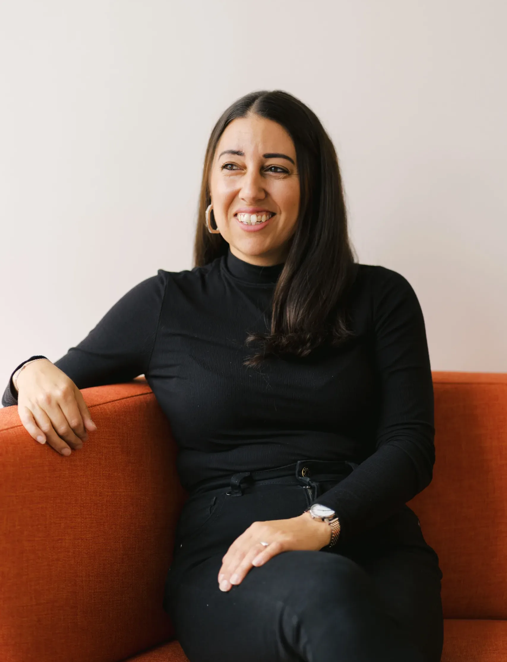 Gemma McCrory smiles while sitting on an orange couch.