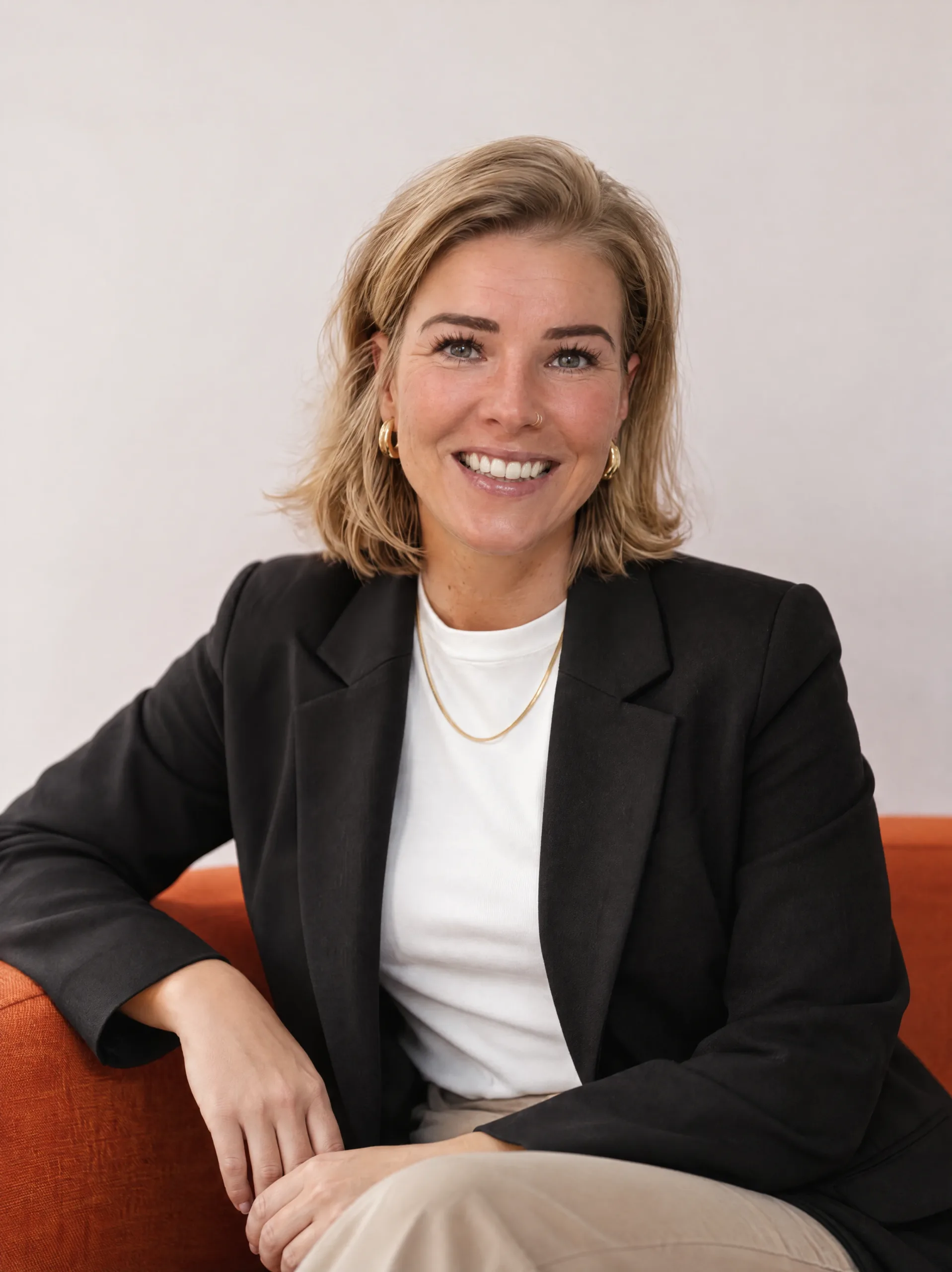 Sarah Muerkl smiles forward, wearing a black blazer over a white t-shirt and gold necklace.