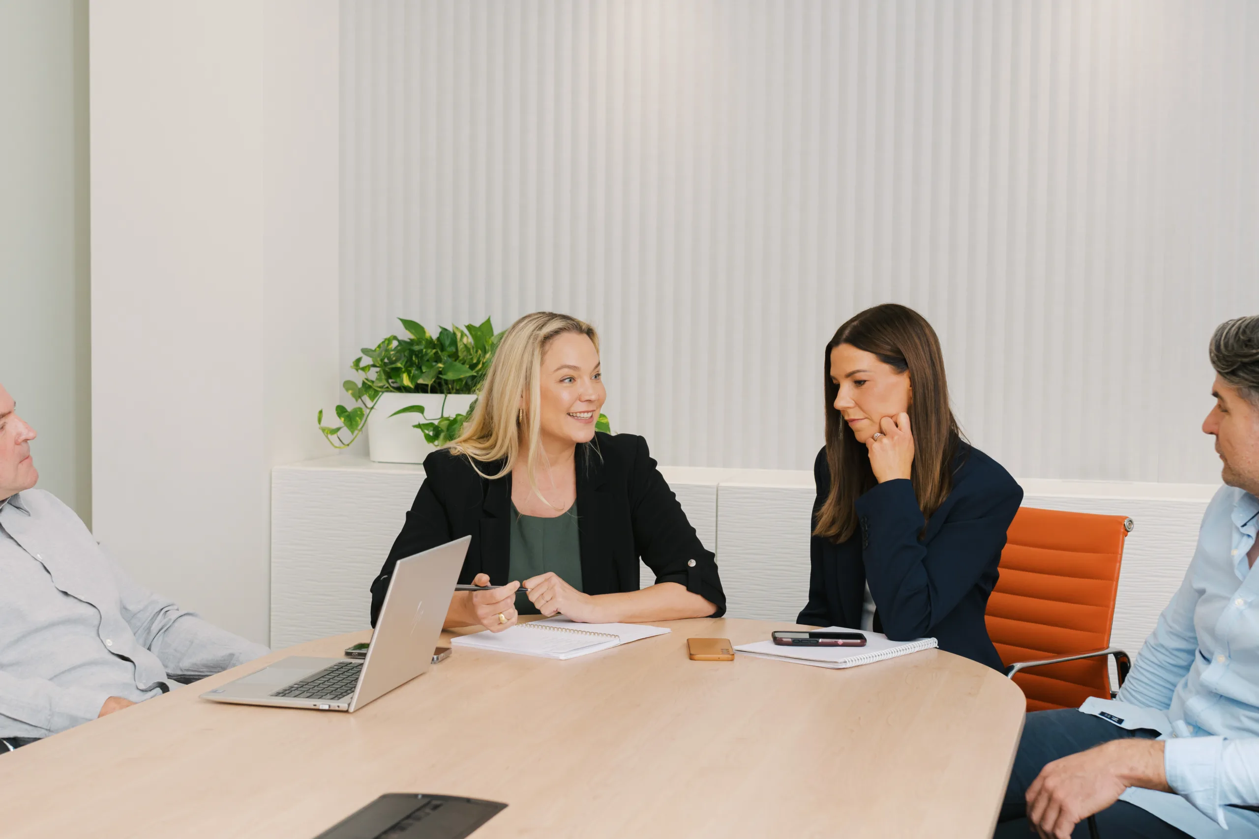 Team members in a meeting discussing strategy around a table with a laptop and notebooks.