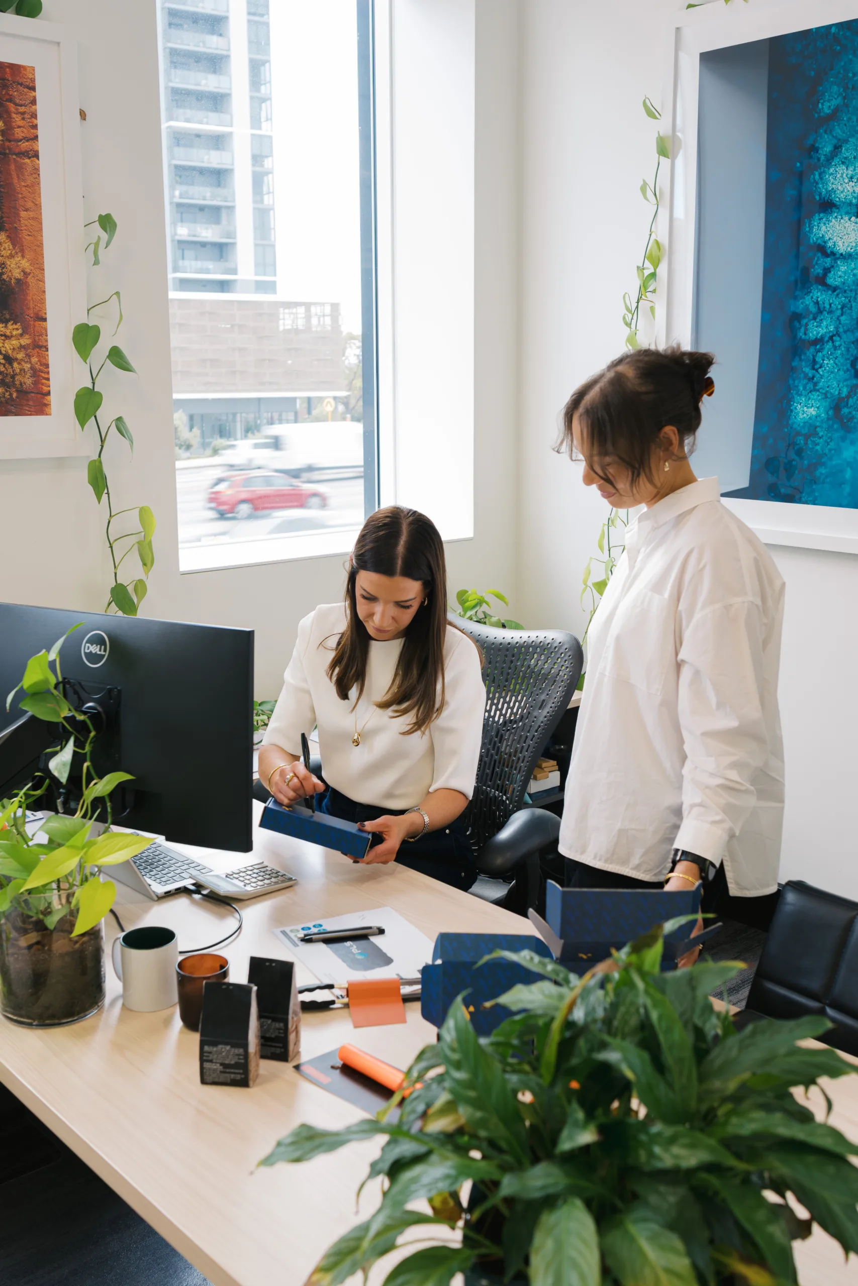 Two women collaborate at a desk with samples and boxes, reviewing materials.