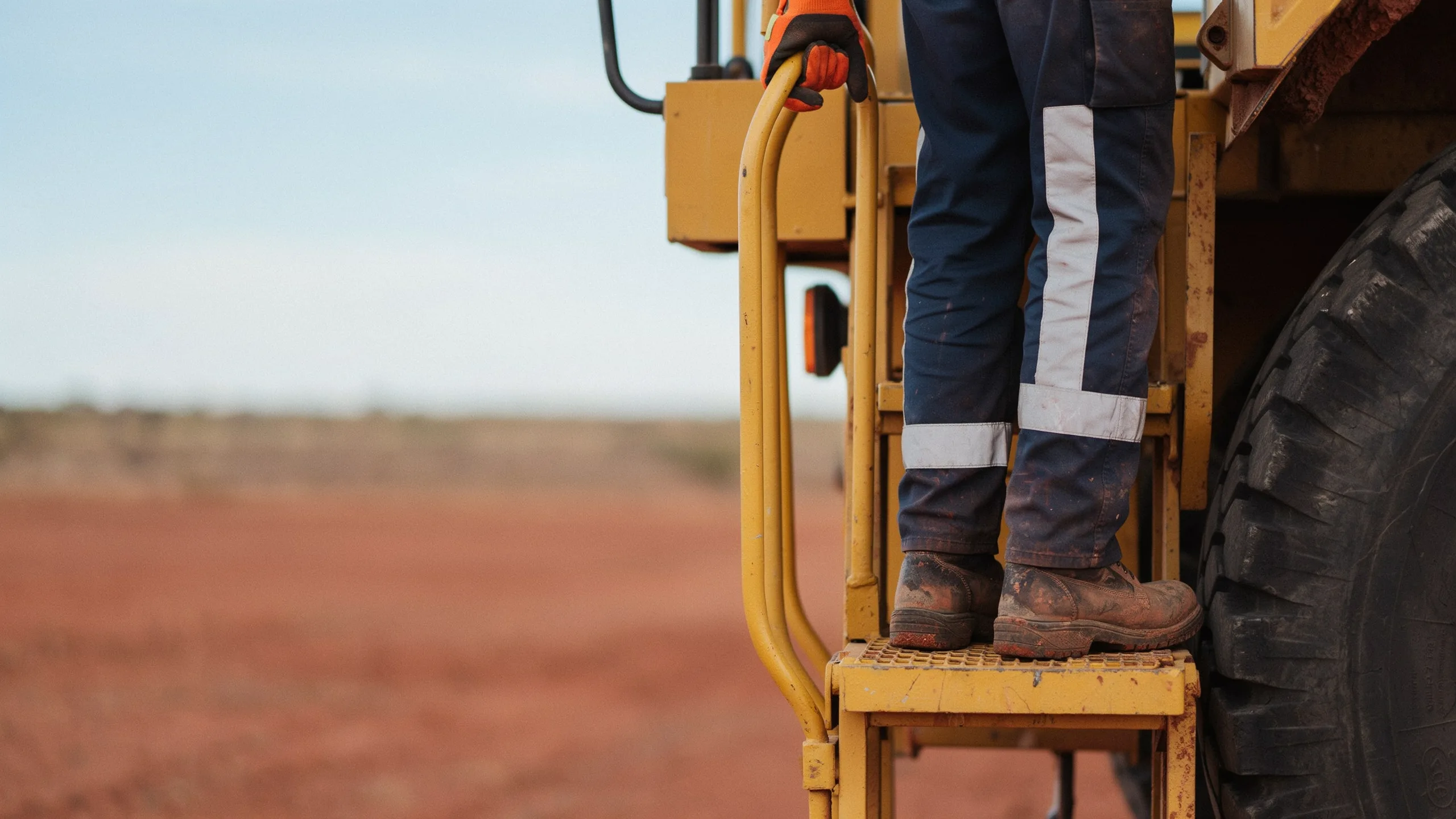 Worker in safety gear climbing steps of large yellow mining vehicle.