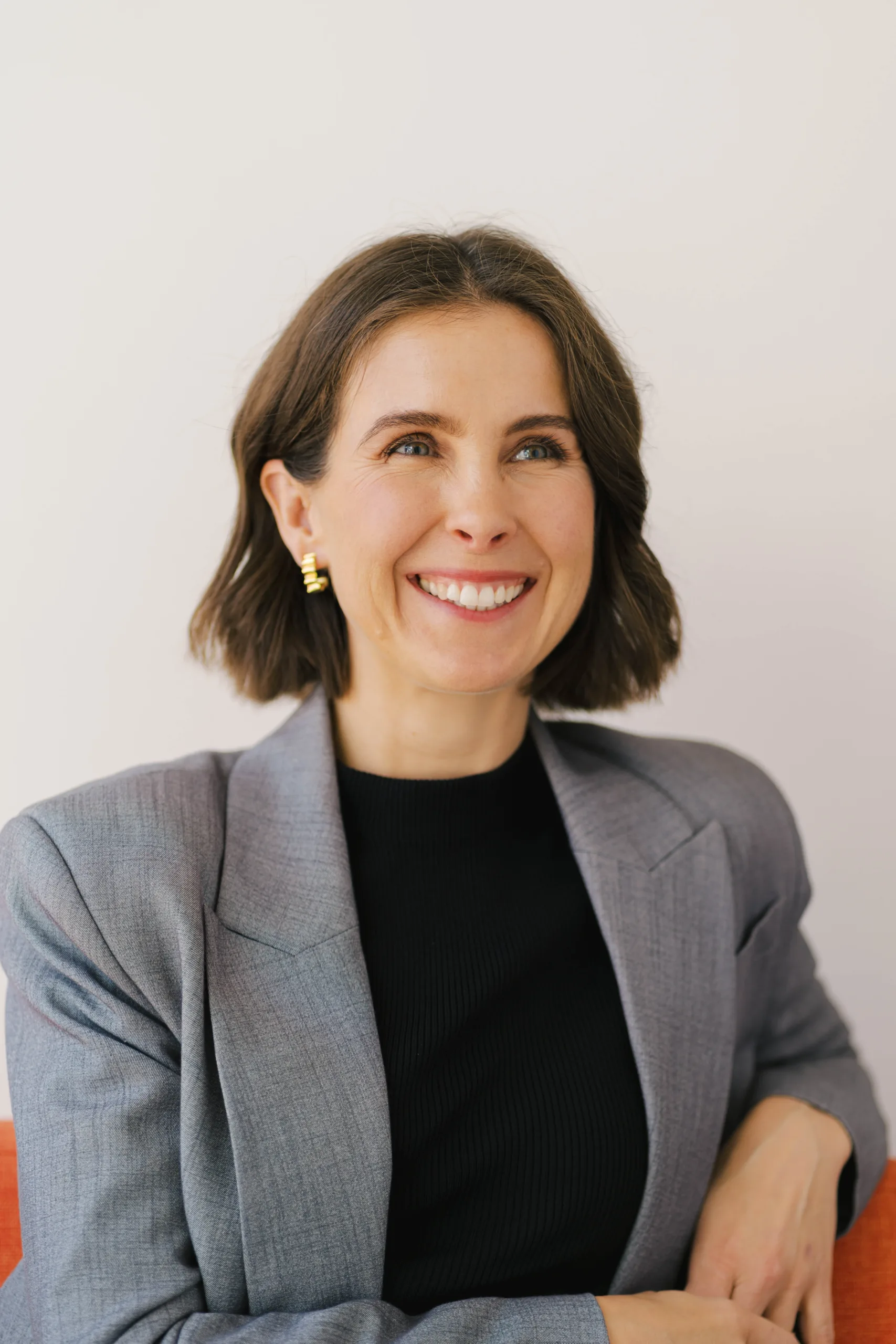 Claire Davies smiles and looks up, wearing a grey blazer and black top.