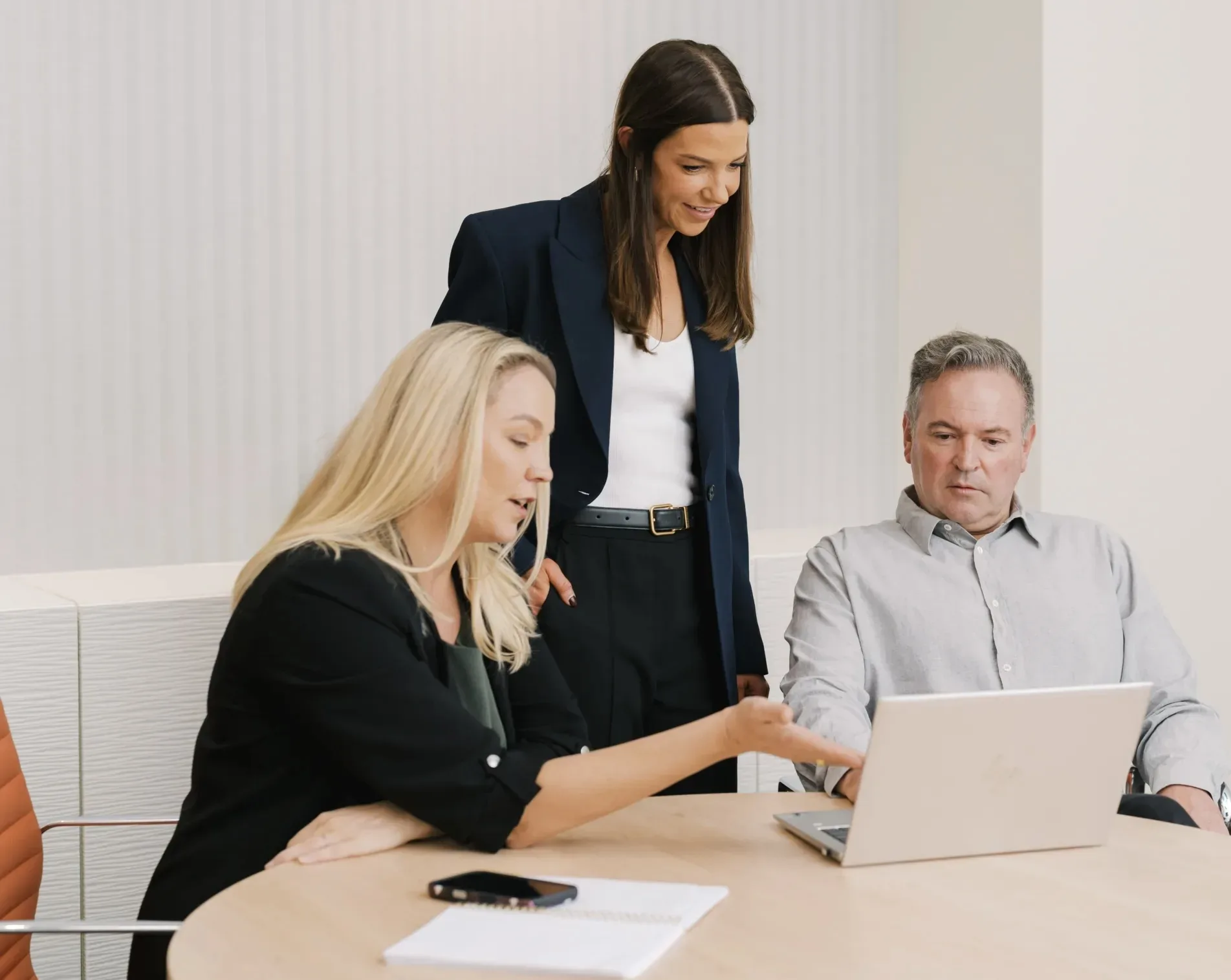 Three professionals collaborate around a laptop in a modern office setting.