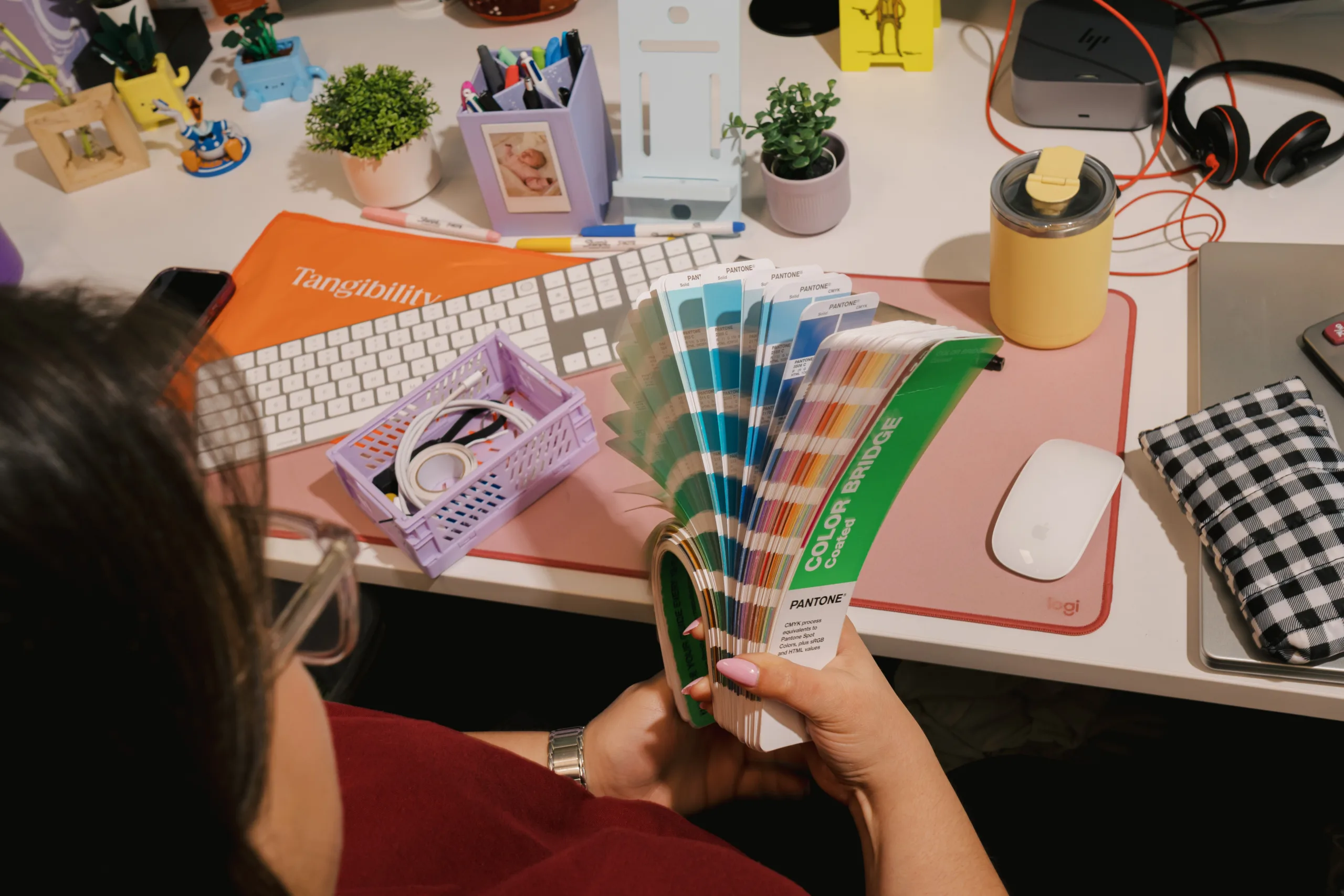 Person holding a Pantone Color Bridge fan deck over a desk with a keyboard and mouse.
